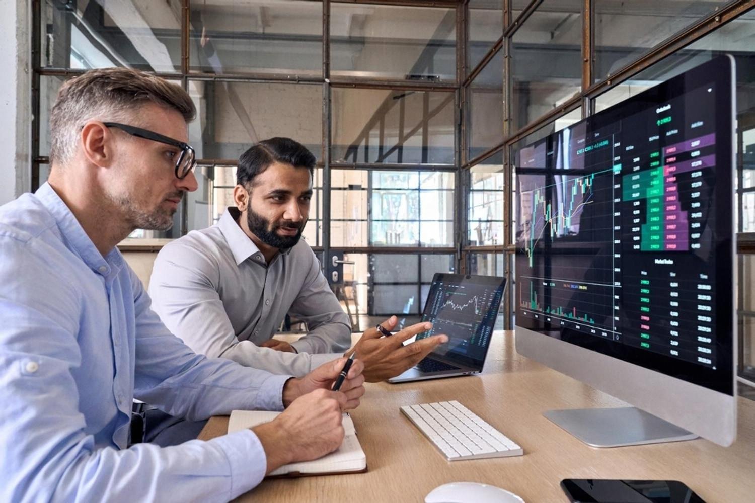Two UAE entrepreneurs analysing investment portfolio charts on a monitor