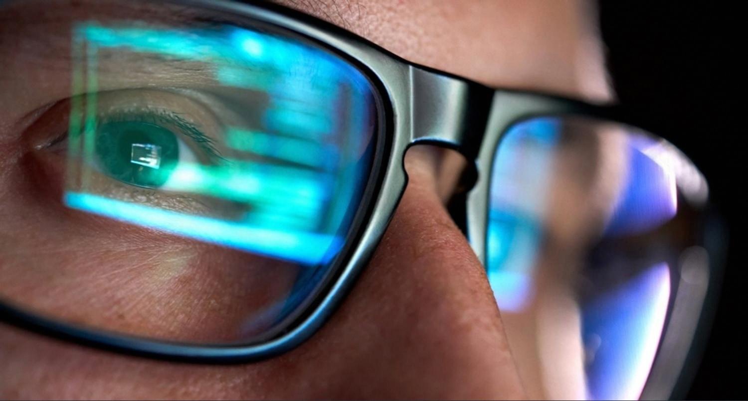 Close-up of an IT specialist reviewing system monitoring dashboards reflected in glasses
